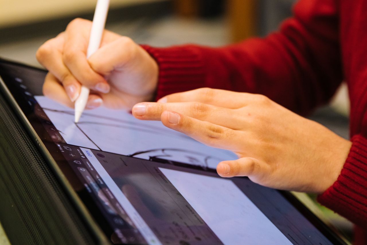 Hands creating digital art with a stylus on a tablet in an indoor setting.